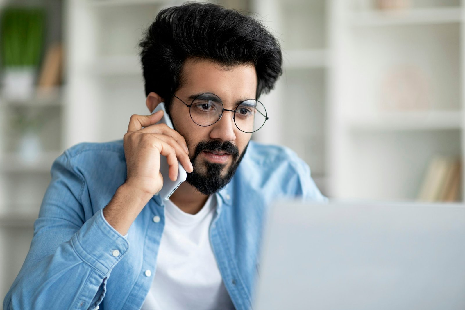 Confused Indian Man Looking At Laptop Screen And Talking On Cellphone, Closeup